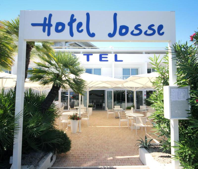 Entrance of Hotel Josse in Antibes, framed by white pillars and surrounded by lush Mediterranean greenery.