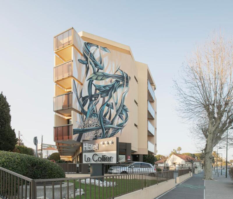 Exterior of Hotel Le Collier, a modern multi‑storey building featuring a large artistic mural in an urban Antibes setting.