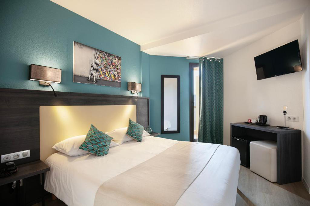 Bright guest room at Hotel Le Collier featuring white linens, a wall‑mounted TV, and a teal‑coloured interior.
