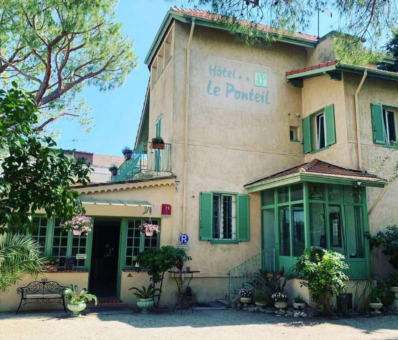 Exterior of Hotel Le Ponteil, a charming light‑coloured building with green shutters surrounded by lush garden greenery.