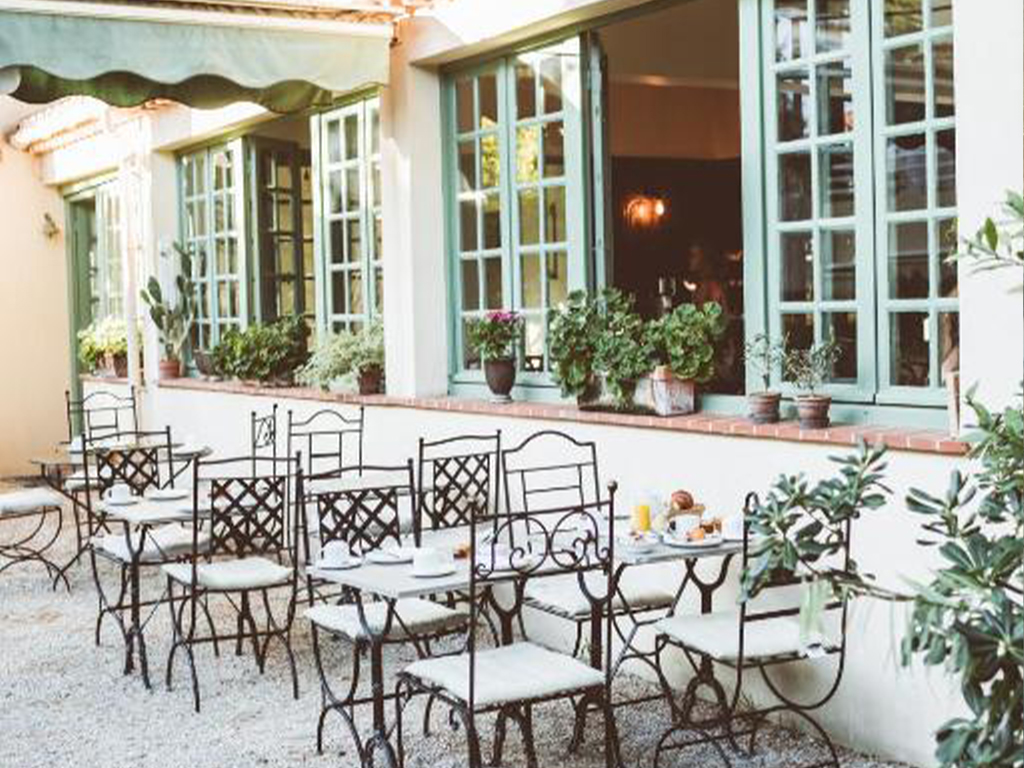 Outdoor terrace at Hotel Le Ponteil with metal tables and chairs set in front of large windows.