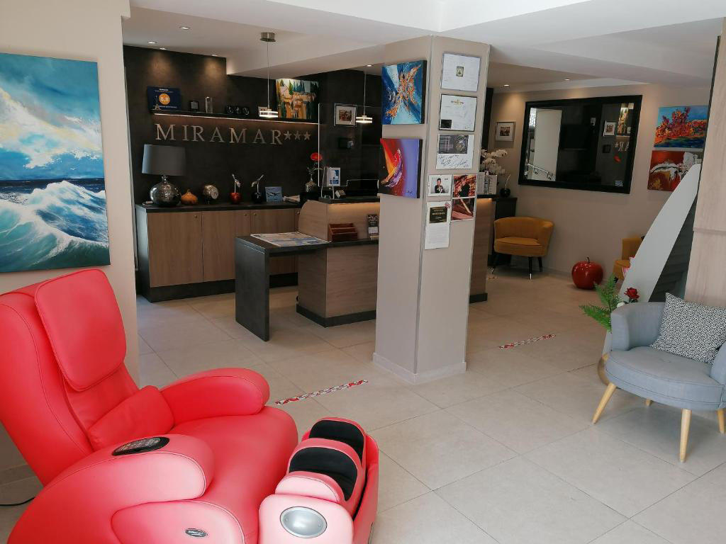 Lobby of Hotel Miramar with a red armchair, modern reception desk, and coastal‑themed artwork.