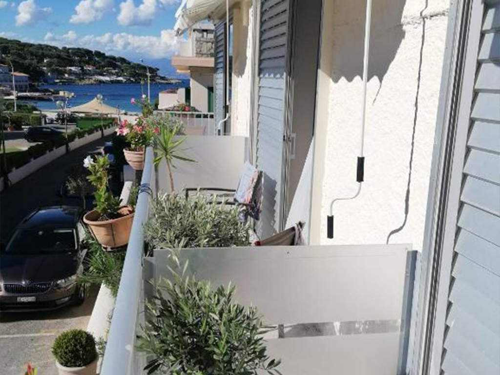 Hotel Miramar room balcony with potted plants and a view of the coastline, parked cars, and surrounding buildings.