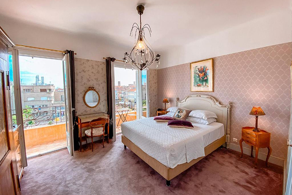 Hotel Relais du Postillon room with a double bed, chandelier, wooden furniture, and a balcony view.
