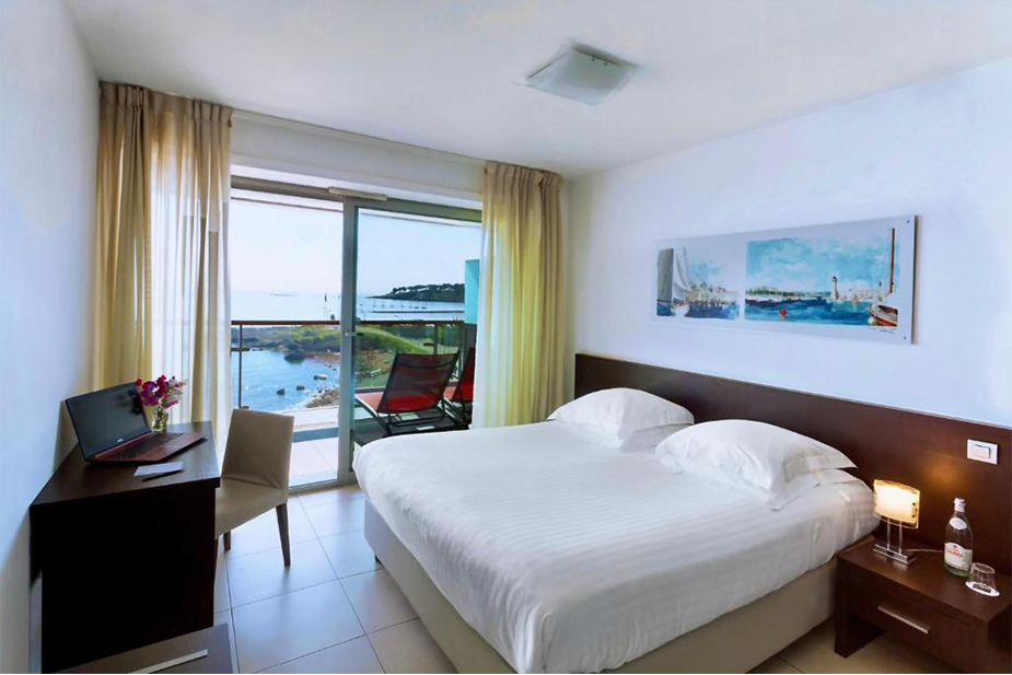 Contemporary bedroom at Hotel Royal Antibes with a neatly made bed, modern furnishings, and a sea‑view balcony.