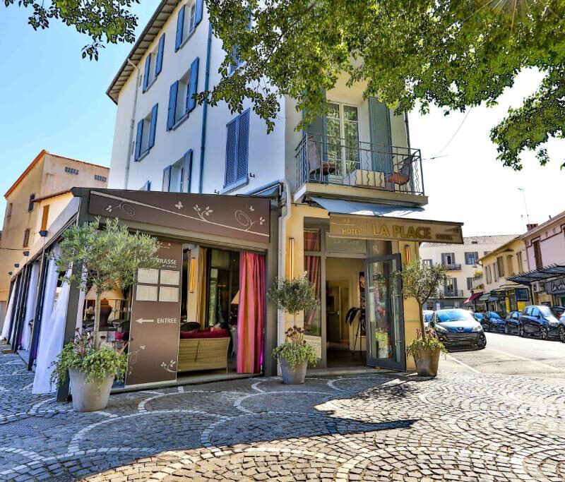 Exterior of La Place Boutique Hotel with its charming façade, cobblestone street, and outdoor seating surrounded by greenery.