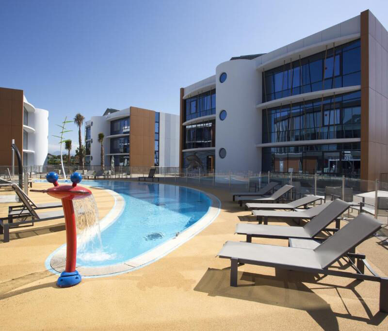 Outdoor pool area at SoBlue Hotel with sun loungers, modern buildings, and a relaxed resort atmosphere.