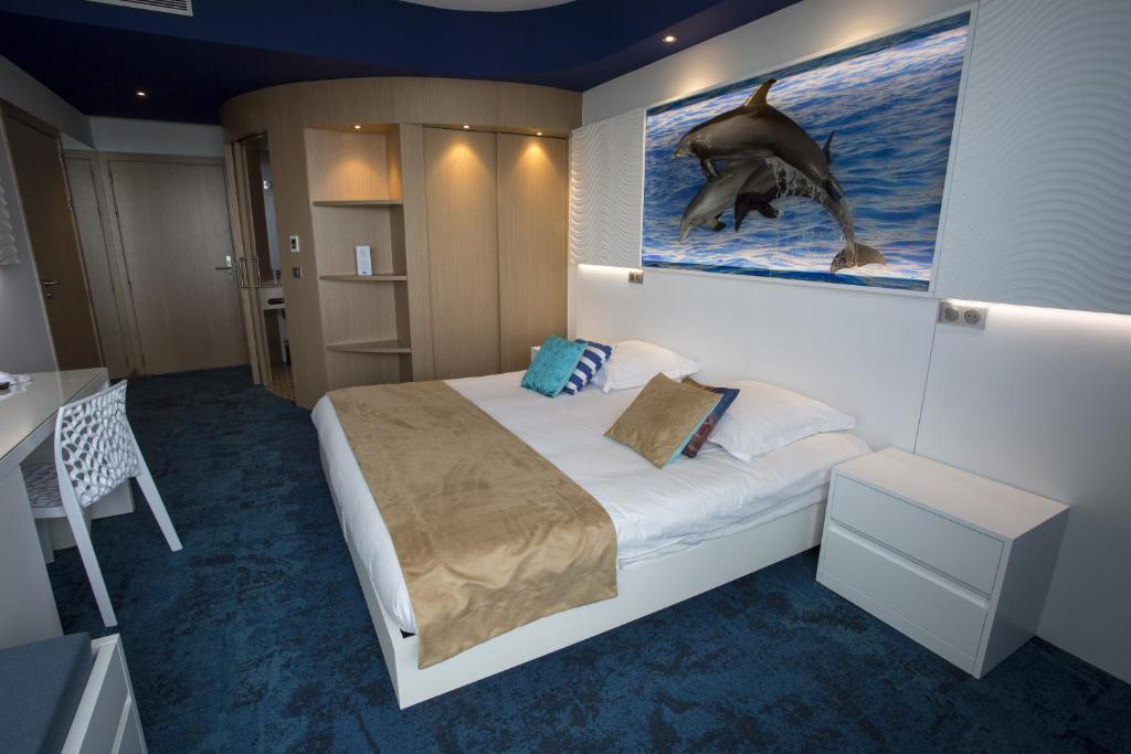 Guest room at SoBlue Hotel with a double bed, beige linens, and marine‑themed wall art.